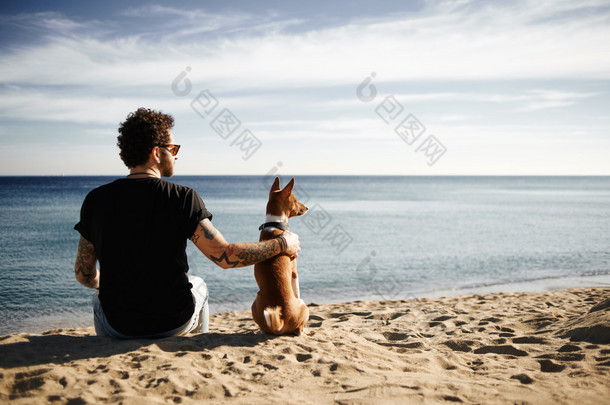 高加索人坐在海滩与朋友一只狗的太阳镜