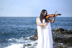年轻有魅力的女人拉小提琴的海面背景