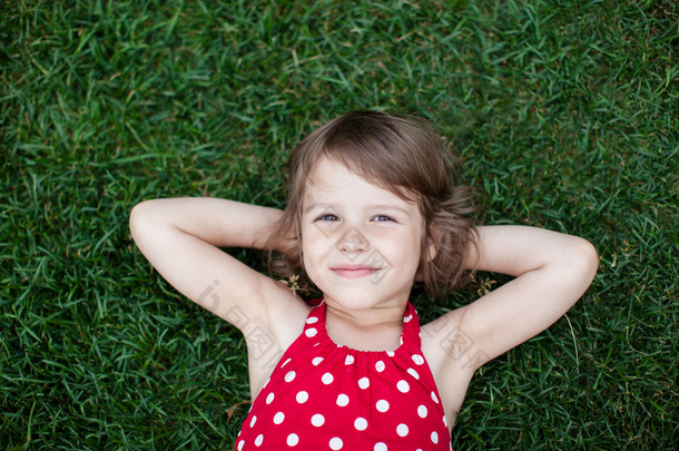 一个微笑的小女孩躺在绿草上的画像