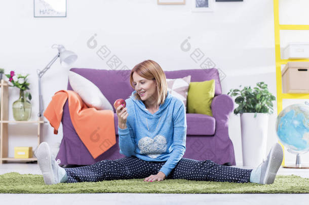 年轻的红头发女人坐在地板上拿着一个苹果