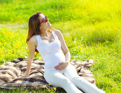 孕妇在休息坐在阳光下草地上的太阳镜