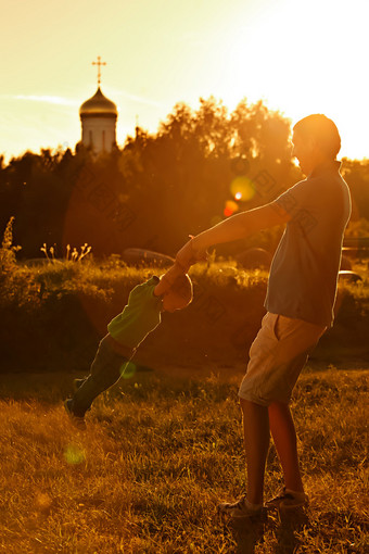 在教会的背景上与他的儿子在公园里玩的快乐老爸.图片