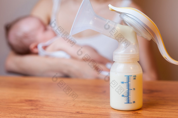 Manual breast pump with milk, mother and baby at background