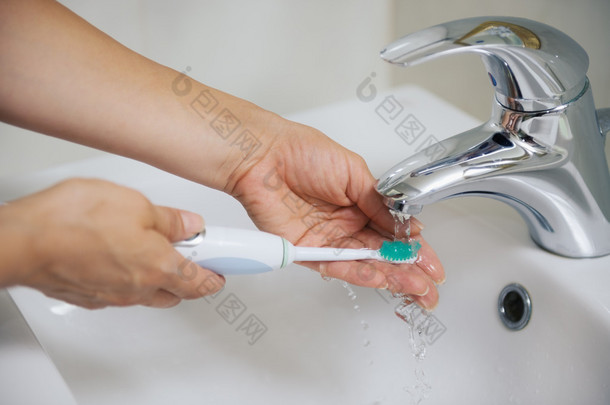 手在水流下清洗电动牙刷上特写