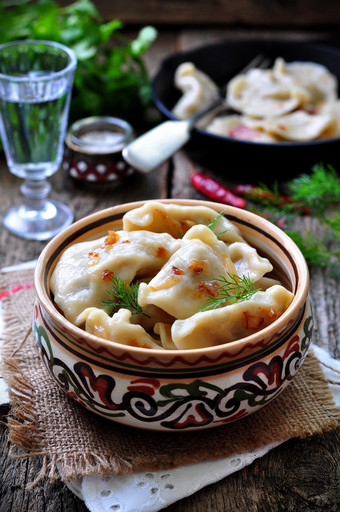 Dumplings with potatoes and mushrooms with fried onions in a traditional ceramic plate on a wooden t图片