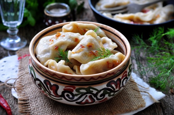 Dumplings with potatoes and mushrooms with fried onions in a traditional ceramic plate on a wooden t