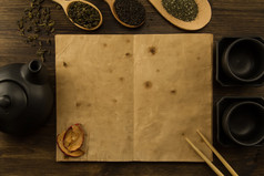 黑茶壶, 两杯, 茶收藏, 鲜花, 木制背景上的旧空白打开书。菜单, 食谱, 模拟