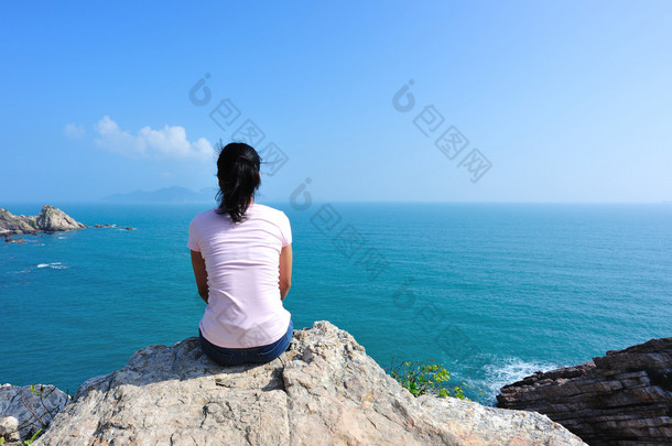 后面的女人坐在海边的岩石上