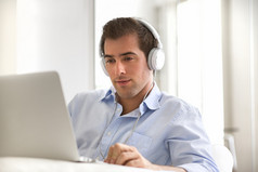 年轻的帅小伙与笔记本电脑使用耳机的肖像