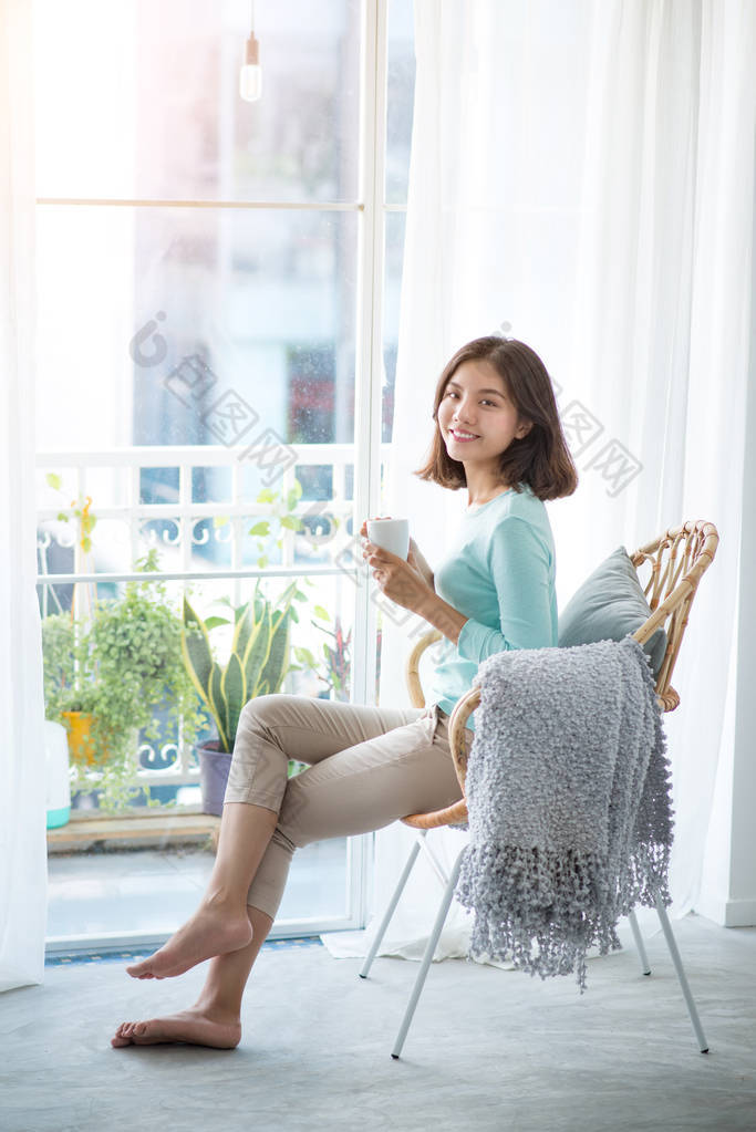 年轻漂亮的女人坐在打开的窗口，喝咖啡和 