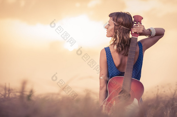 在她身后欣赏落日美景的原声吉他的年轻女子 