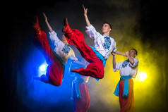 四个年轻人在乌克兰民族服饰舞蹈在黑暗的背景与烟