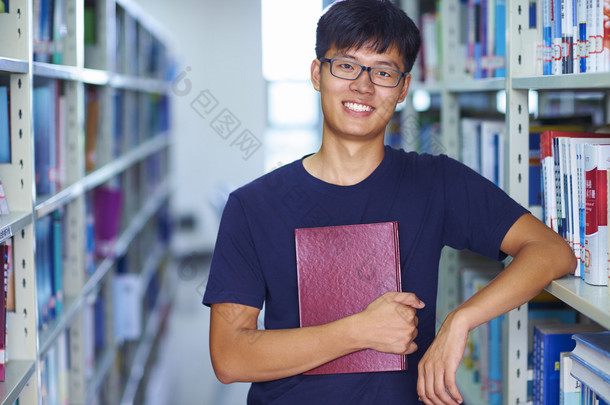 年轻的男大学生看图书馆中的相机微笑