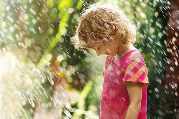 快乐的小女孩站在夏天的雨下的照片