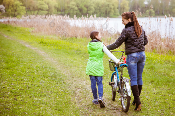 女儿和母亲与一辆自行车湖岸边走路和说话。家庭价值观教育
