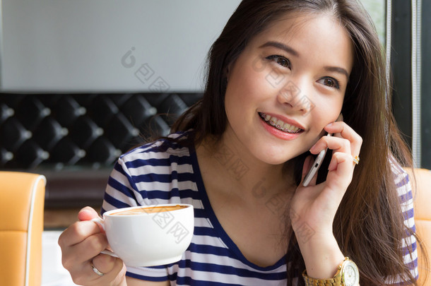 美丽的女人谈电话，拿着杯咖啡