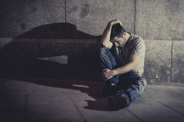 沮丧的年轻人坐在街道的地面上与混凝土墙上的影子