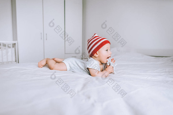 婴儿在红色和白色条纹帽与绒球玩玩具鹿在床上