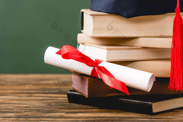 书籍，学术帽和文凭的木制表面隔离在绿色