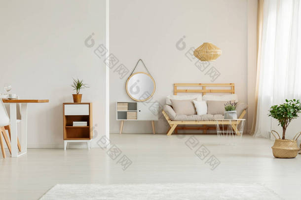 镜子在白色内阁旁边在米色木沙发在客厅内部与植物。真实照片