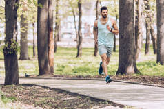 穿着运动服的帅哥在阳光明媚的公园里沿着人行道奔跑
