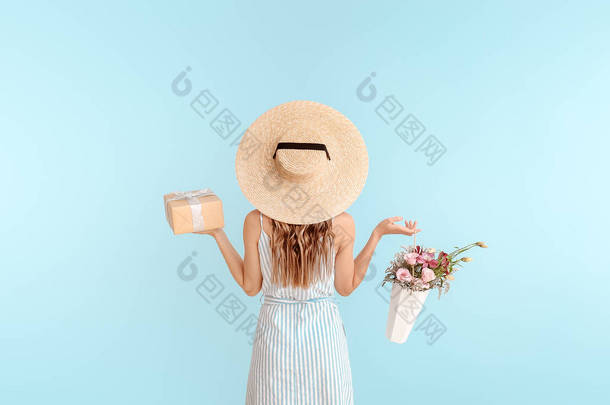 美丽的年轻女子与礼品盒和鲜花在浅色背景，后视图