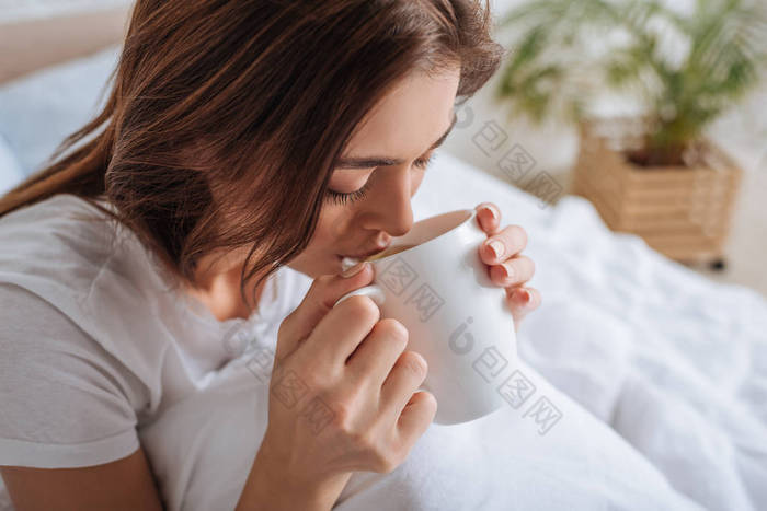 迷人的年轻女子在卧室喝茶 