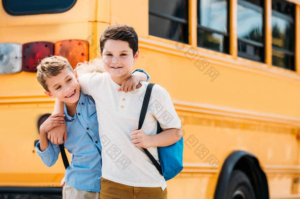 微笑的小男生拥抱在校车前 