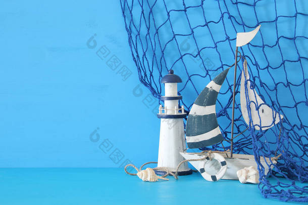 航海概念以白色装饰风帆小船、灯塔、海贝壳和鱼网在蓝色木桌和背景.