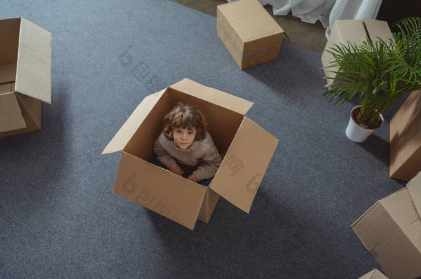 小男孩的高角度的看法坐在箱子和看在照相机在迁移期间
