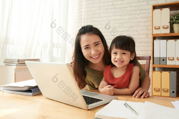快乐的亚洲母亲与她的小女儿在桌子上的笔记本电脑