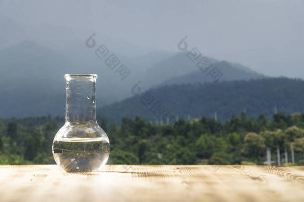 在山背景<strong>上</strong>木制的桌子<strong>上</strong>的玻璃实验室瓶的清洁水。生态概念，纯度和质量的水试验.