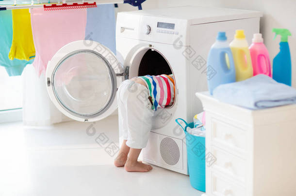 儿童在洗衣房内设有洗衣机或滚筒烘干机。帮助家庭琐事的<strong>孩子</strong>。现代家庭设备和洗涤洗涤剂在白色阳光的家。烘干机架清洗洗<strong>衣服</strong>. 