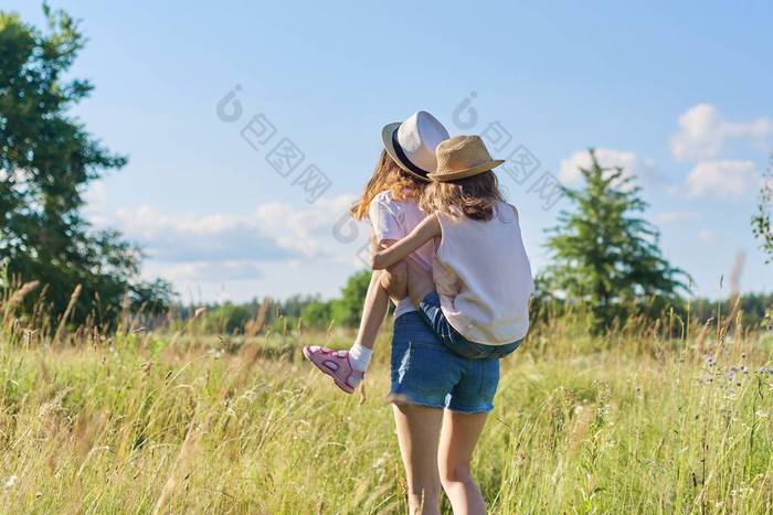 快乐的孩子，两个女孩妹妹，一个是少女，一个是少女，另一个是少女，笑着，在草地上玩的开心，蓝天，夏天的自然。积极健康的生活方式，友善的家庭，快乐的童年，复制的空间