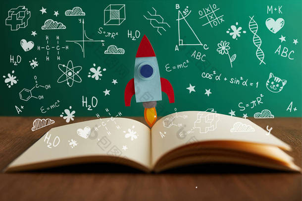 打开书与五颜六色的火箭在木桌与数学图标