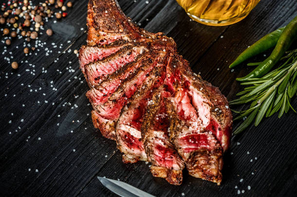 烧烤干岁的肋的牛肉、 香料、 蔬菜以及一杯淡啤酒特写黑色木制背景