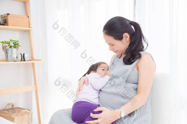 怀孕的亚洲母亲母乳喂养她的女儿在家