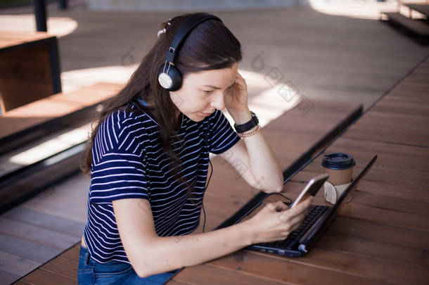 一个带着智能手机的女学生，坐在笔记本电脑前，用耳机仔细听，学习<strong>外语</strong>.