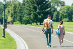 少年男孩和女孩的后面看法与背包和滑板一起走在公园里