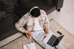 坐在地板上用笔记本电脑的年轻人阅读假新闻报纸的头顶视图