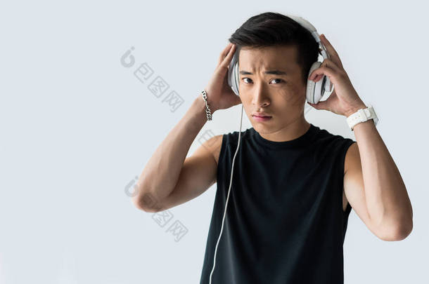 严肃的亚洲运动员戴上耳机在灰色背景下被隔离 
