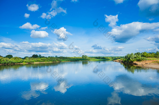 宽阔的河流与反射和绿色布什对海岸和蓝色<strong>多</strong>云的天空