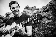 帅气的微笑吉他手玩音乐选址上海滩岩。黑色白色户外写真.