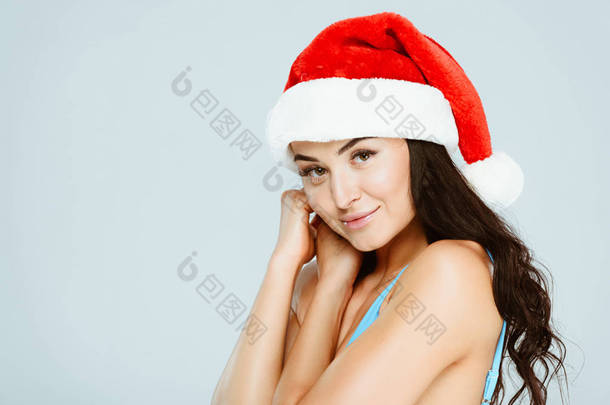 蓝色泳装和<strong>圣诞</strong>帽上的美丽女人的肖像在灰色隔离