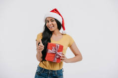 微笑非洲裔美国女孩在圣诞老人的帽子举行目前和显示拇指上孤立的白色