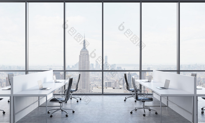 Workplaces in a bright modern open space office. White tables equipped with modern laptops and black