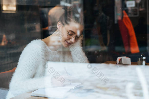 可爱的女孩在白色毛衣和眼镜坐在咖啡馆, 学习后休息