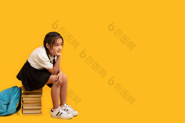 不快乐的女学生坐在书架上，黄色背景，全景