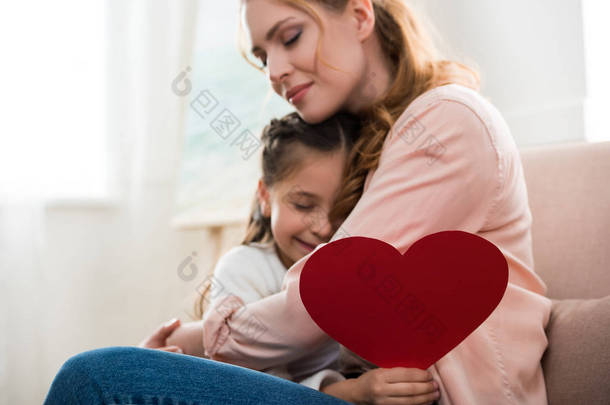 愉快的母亲和女儿以红色心脏标志拥抱在家