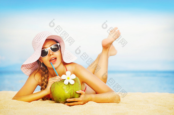 年轻女子在粉红色泳装与椰子鸡尾酒在沙滩上巴厘岛